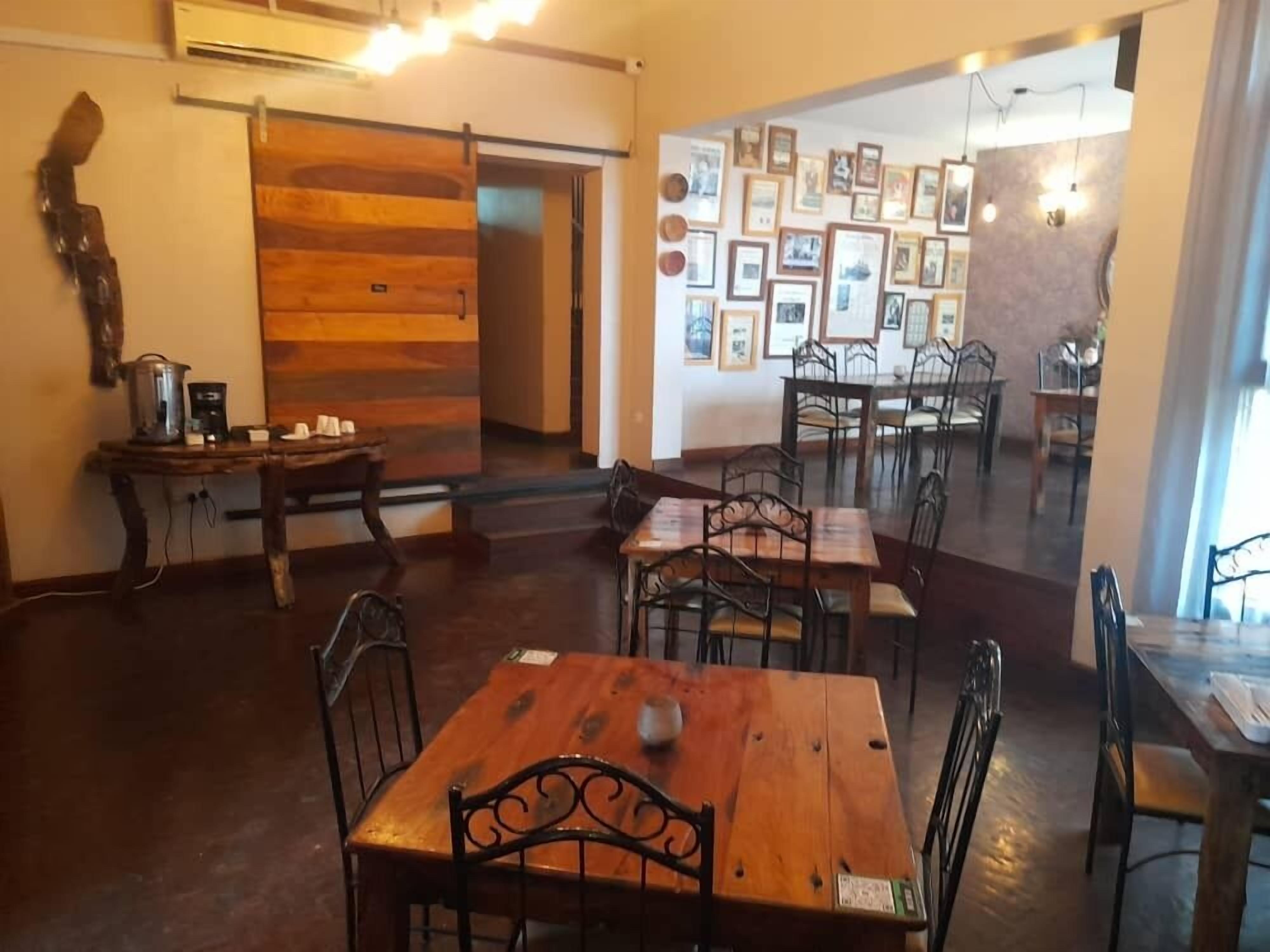 A dining area with wooden tables and chairs, a coffee machine, and a wall decorated with framed pictures.
