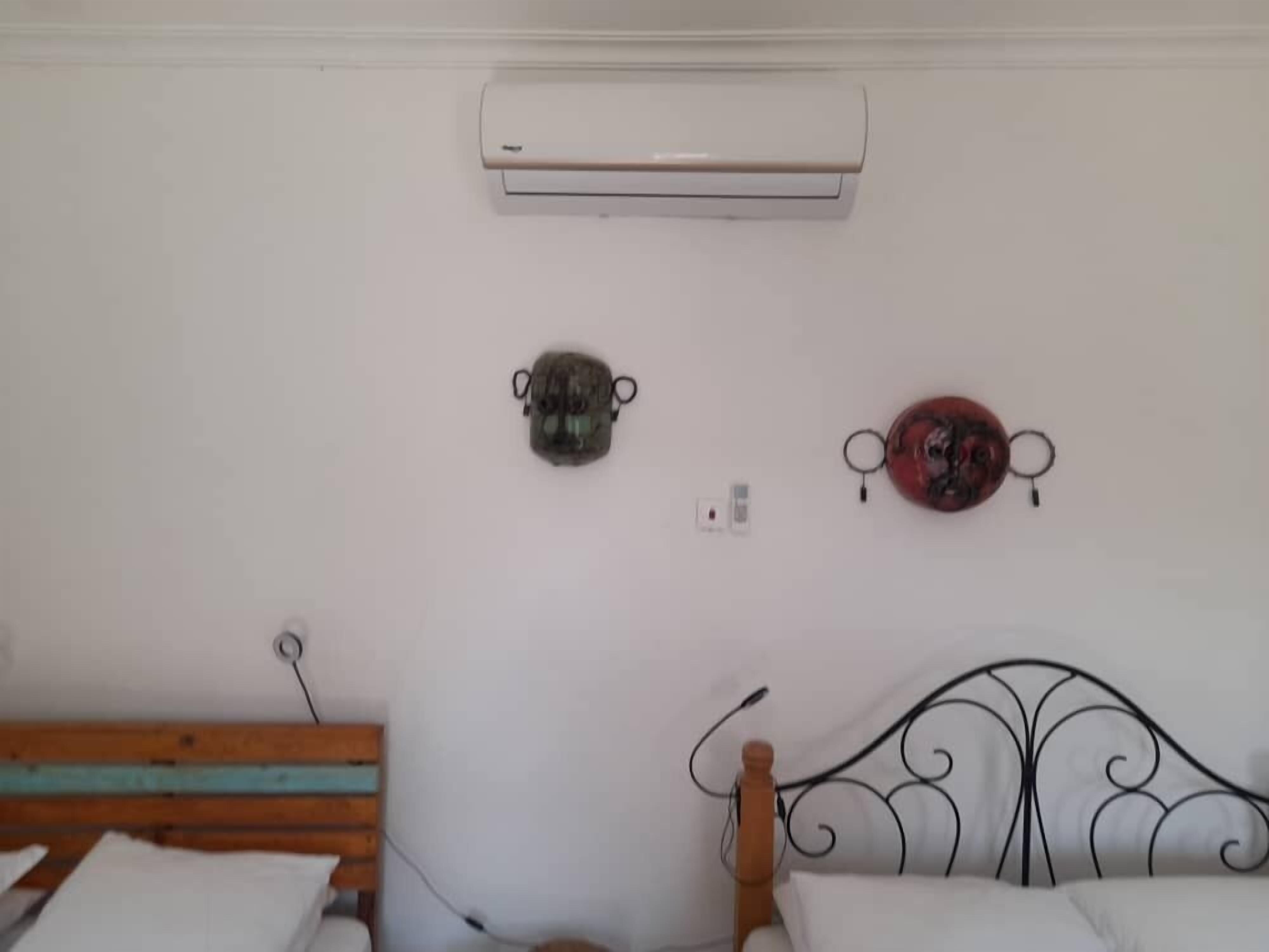 Un dormitorio con una cama de madera, una pared blanca, un aire acondicionado y dos adornos colgados en la pared.