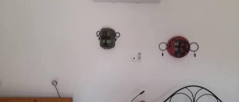 Un dormitorio con una cama de madera, una pared blanca, un aire acondicionado y dos adornos colgados en la pared.