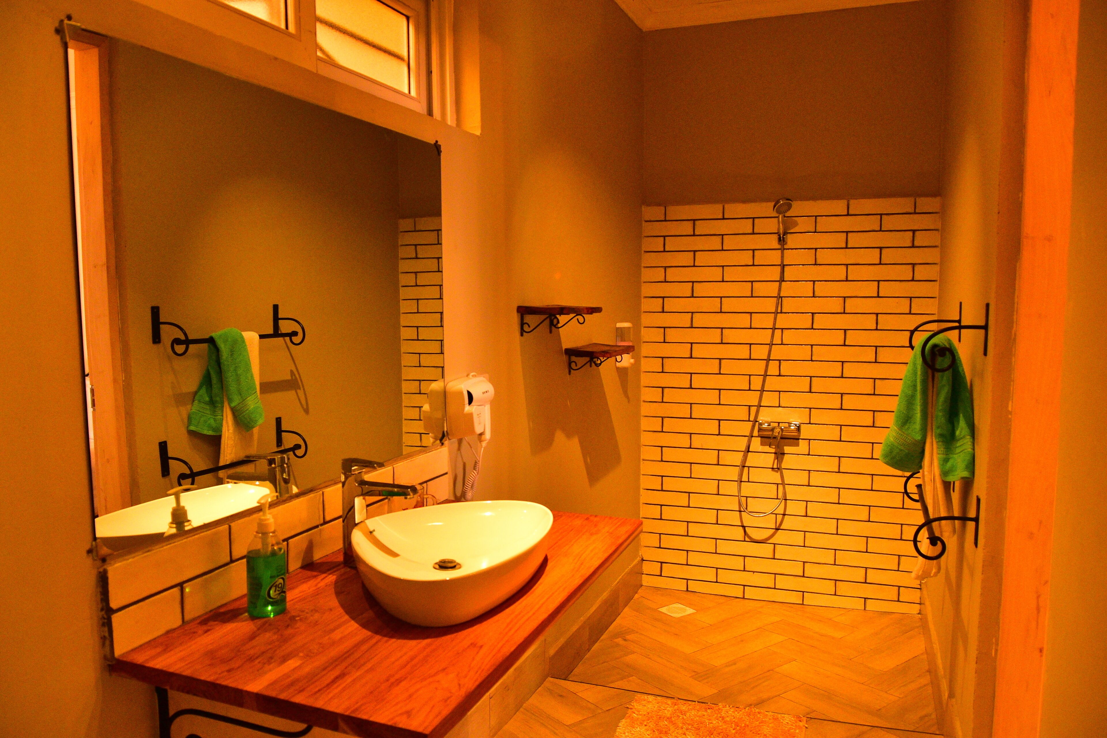 A bathroom with a wooden vanity, a sink, a mirror, a towel rack, and a shower area with a brick wall.