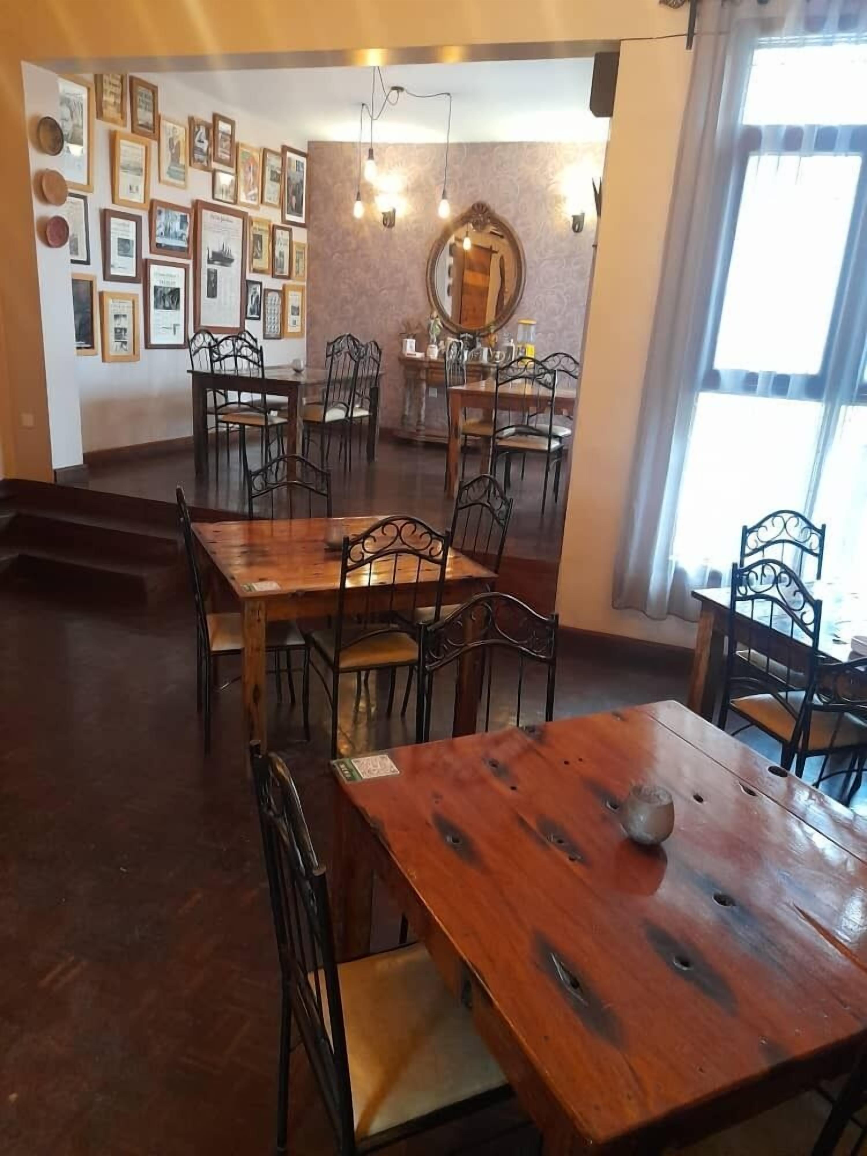 Un comedor con mesas de madera y sillas de metal, cuadros en las paredes y un espejo grande.
