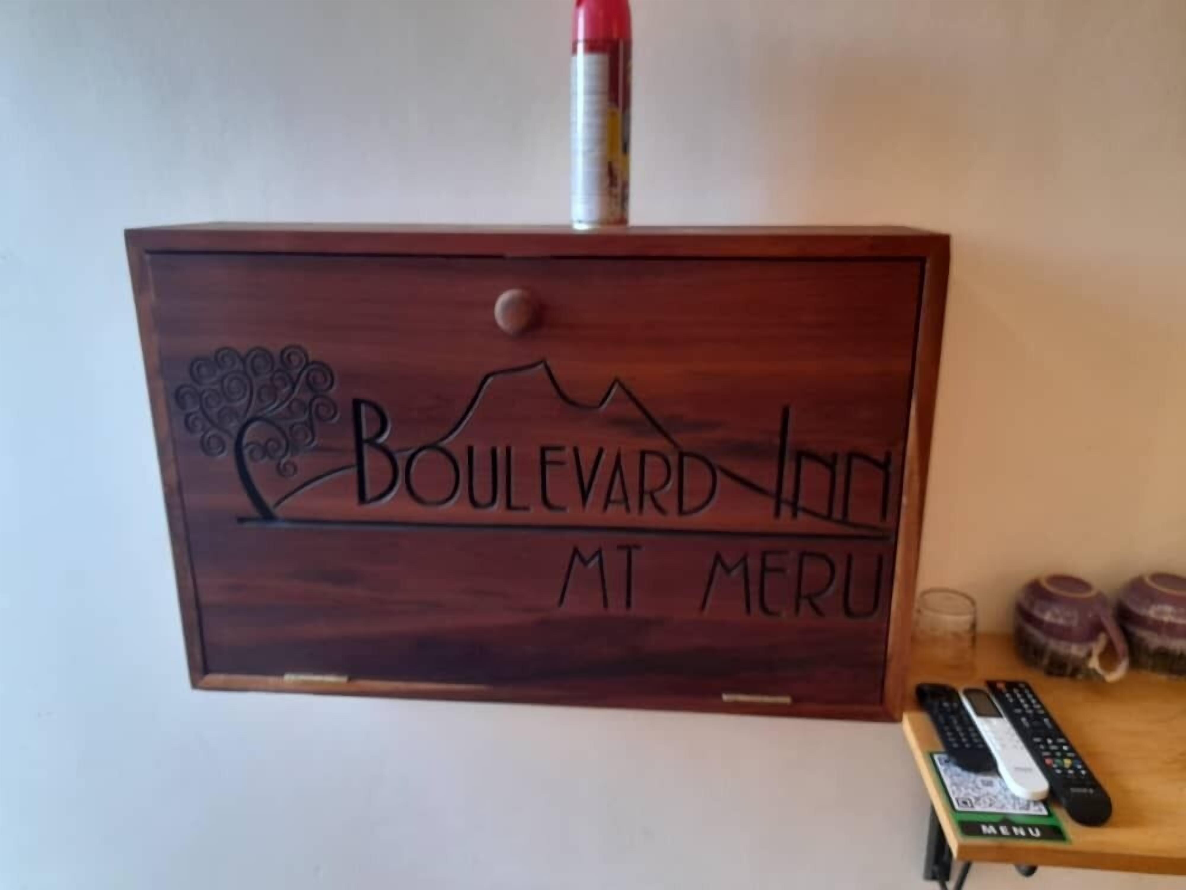 Une enseigne en bois portant l’inscription « Boulevard Inn MT Meru » et représentant un paysage de montagne.