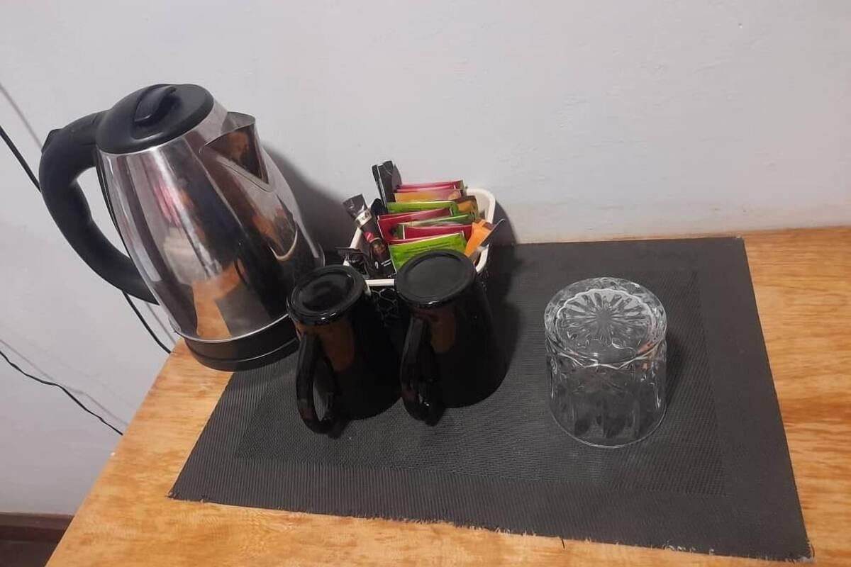 Eine Küchenarbeitsplatte mit einem Wasserkocher, Kaffeekannen, einem Glas und einer Stapel bunter Tassen.