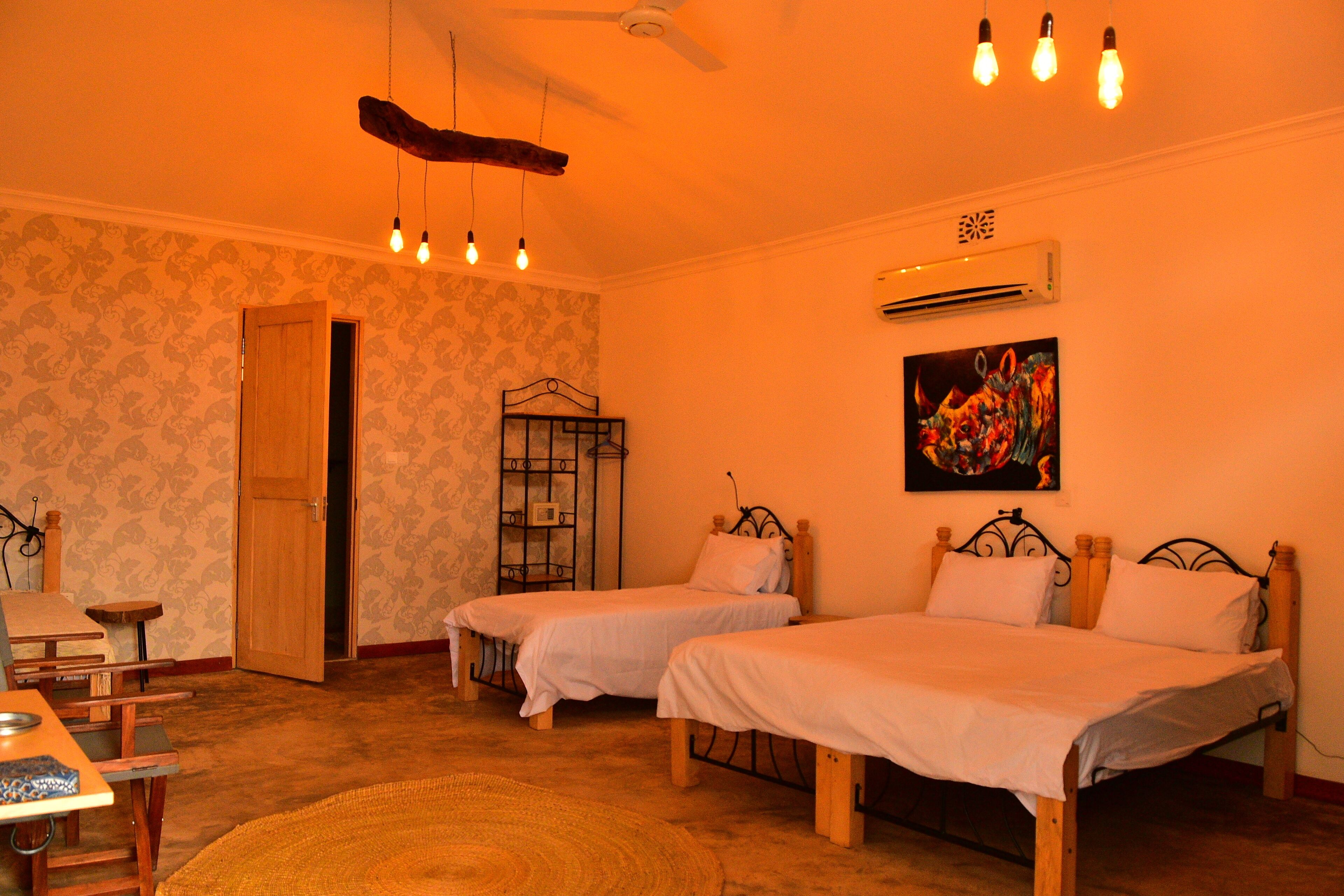 A room with two single beds, a wooden door, a small table, and a wall-mounted air conditioner.
