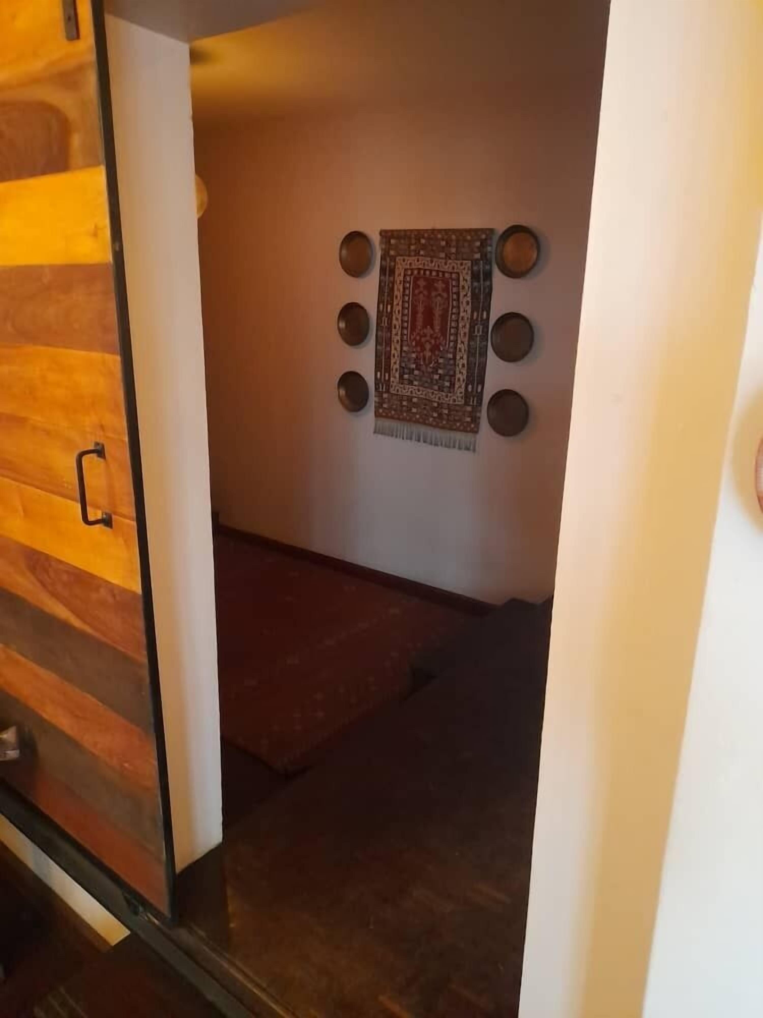 A hallway with a wooden floor, a patterned rug, and a wall-mounted decorative piece with circular elements.