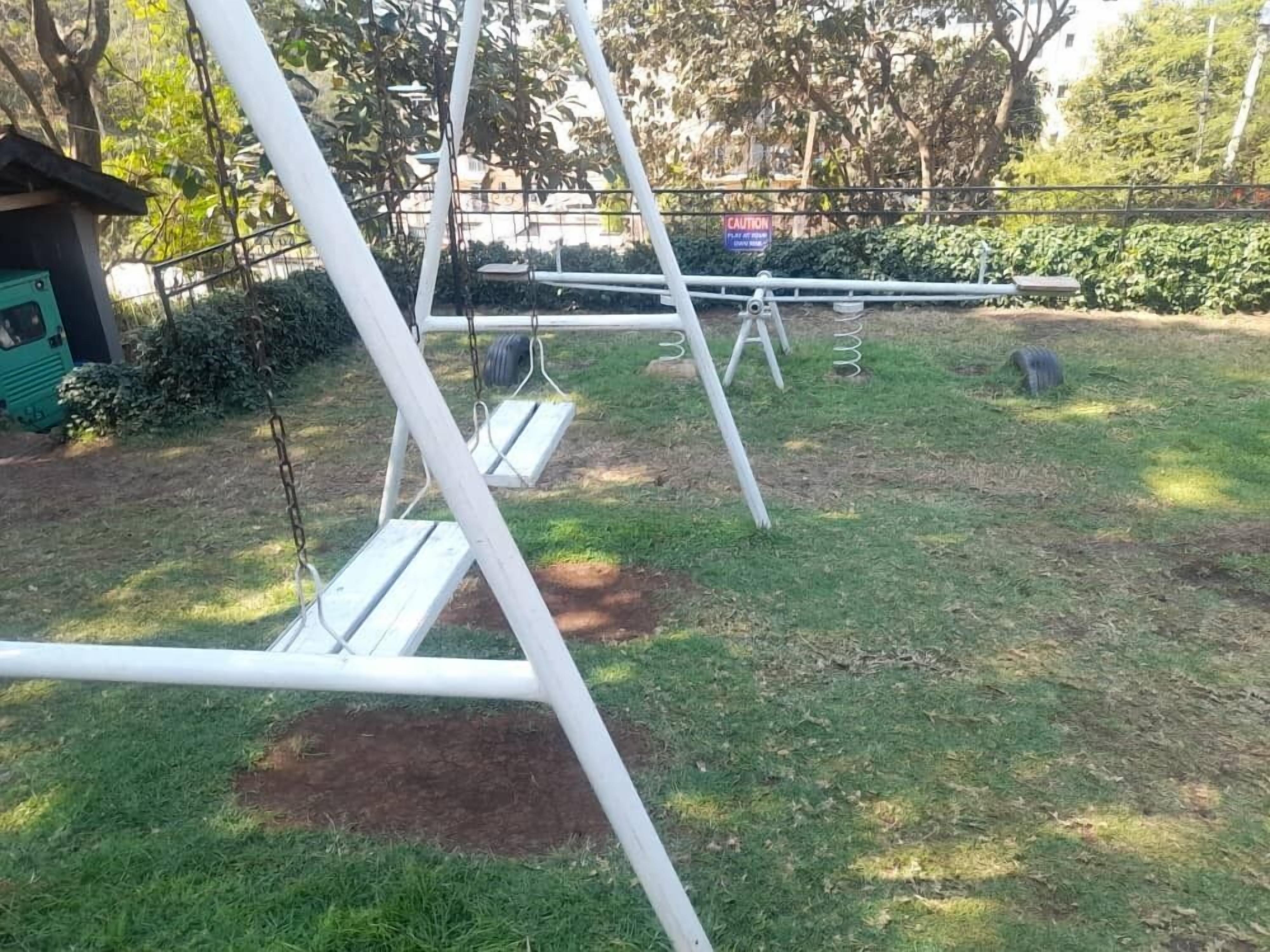 Une balançoire installée dans un espace herbeux, avec un panneau d’avertissement en arrière-plan.