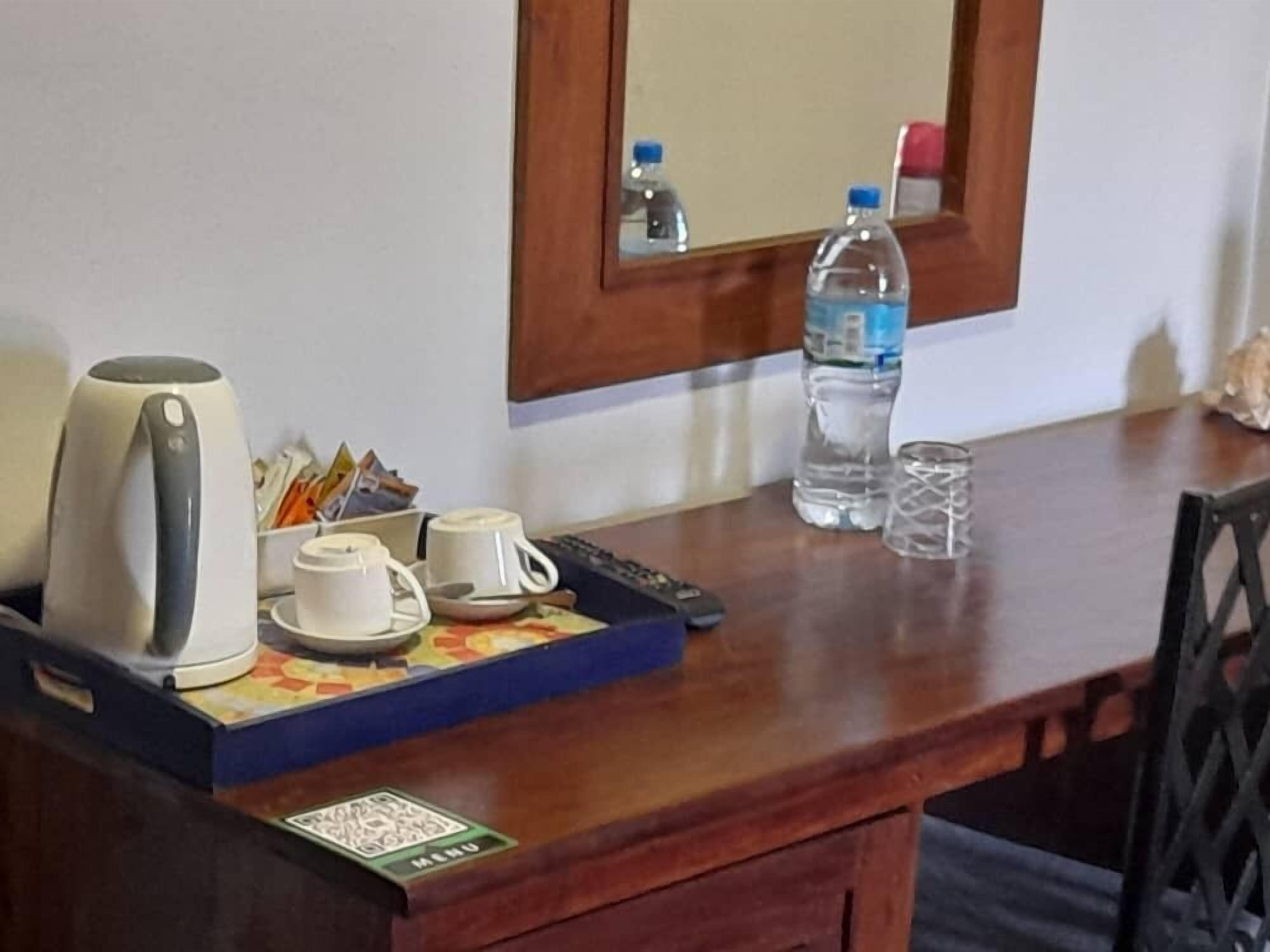 A wooden desk with a kettle, cups, a remote control, a water bottle, and a glass.