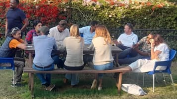 A group of people seated around a wooden table outdoors, with a garden and flowers in the background.