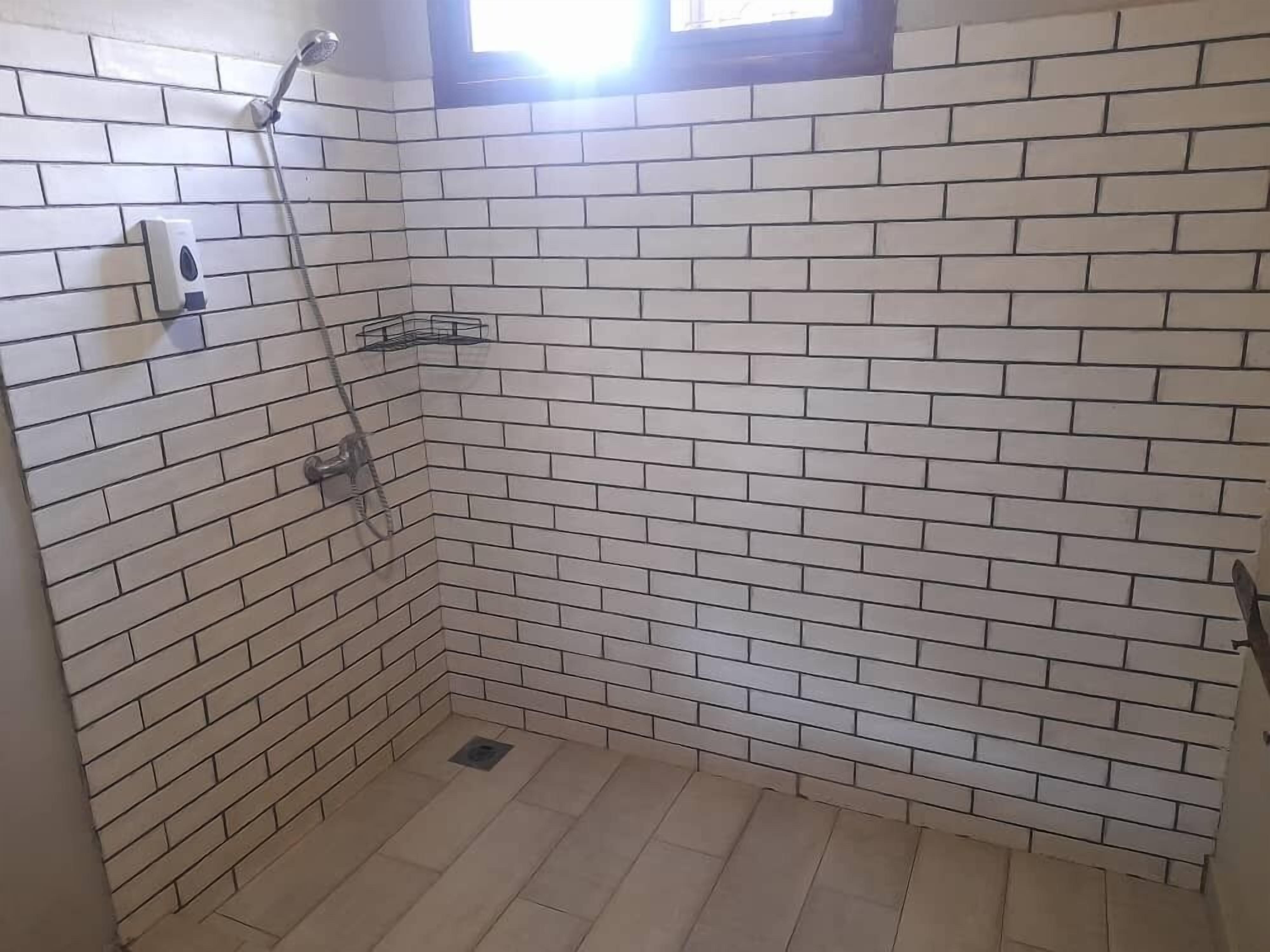 Un piccolo spazio doccia piastrellato con soffione a mano e dispenser di sapone.