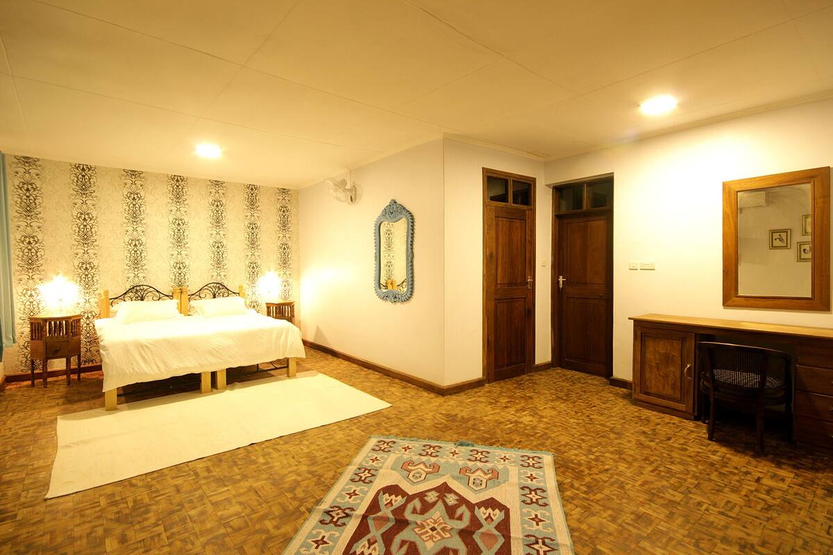 Ein Schlafzimmer mit Bett, Nachttischen, einem Spiegel, einem Kleiderschrank und einem gemusterten Teppich.