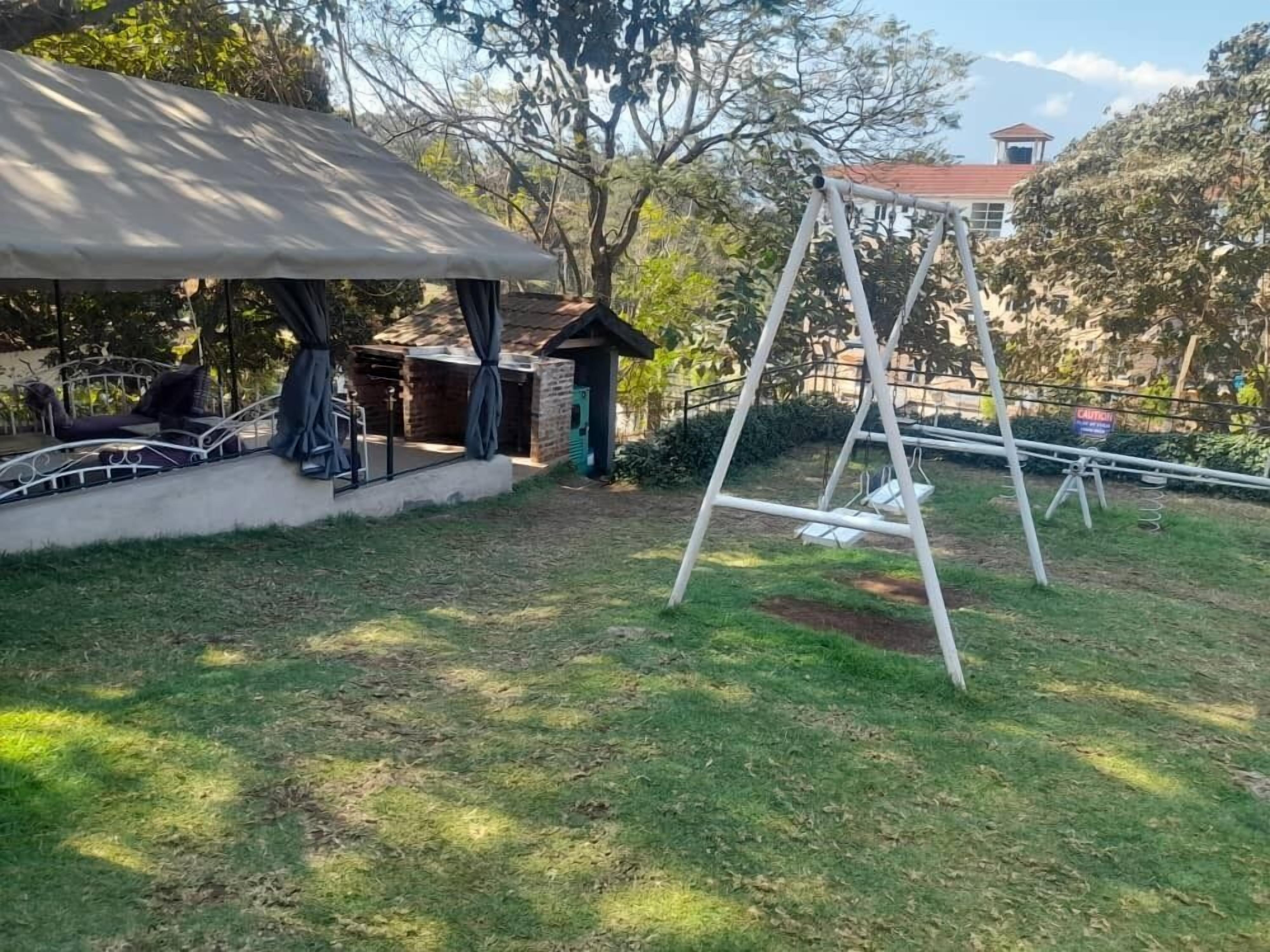 A patio area with a swing set, a covered seating area, and a small brick structure.