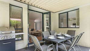 An outdoor dining area with a grill, a table set for four, and a view of the interior.