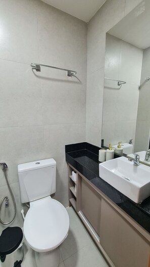 A bathroom with a toilet, sink, and mirror. - Flat Ofurô 17 VP by La Playa (Ipojuca)