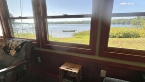 Ein gemütliches Zimmer mit großem Fenster mit Seeblick, einem kleinen Bücherregal aus Holz und einem bequemen Sessel.