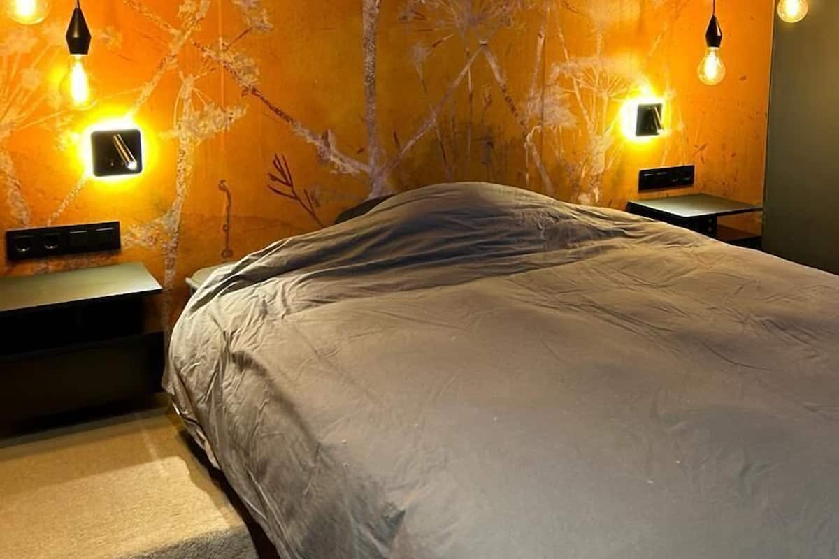 A bedroom with a bed, two bedside tables, and a wall with a tree mural.