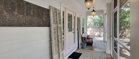 A covered porch with white siding, a vintage sign, a bench, and two hanging lanterns.