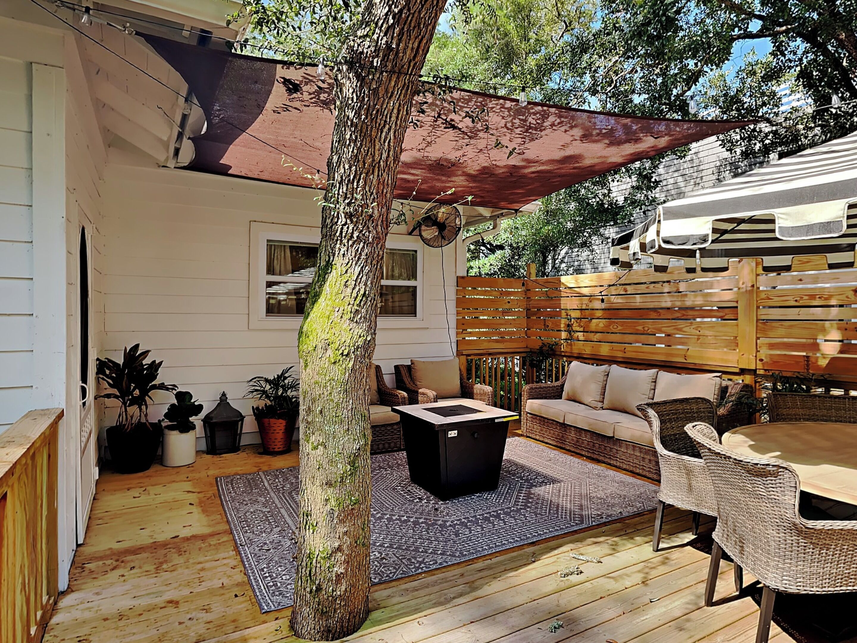 A wooden deck with a covered seating area, a table, and a large tree.