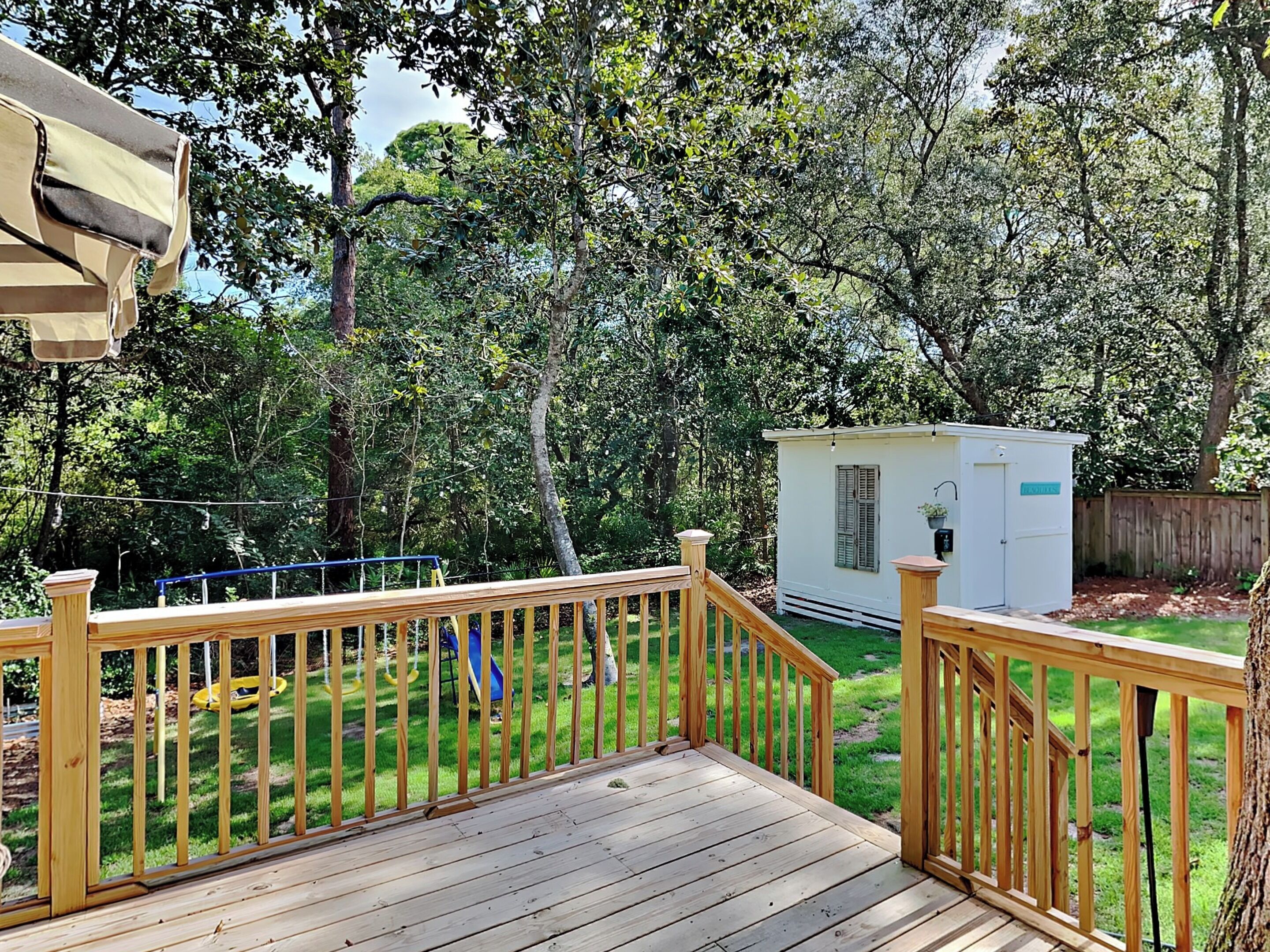 A wooden deck with a railing, a small shed, and a playground with a slide.
