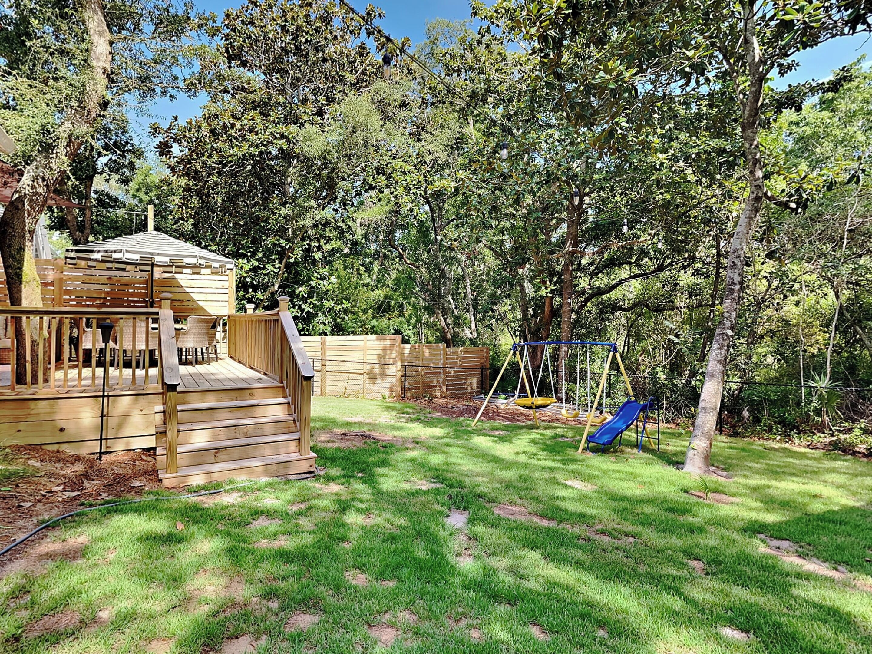 A wooden deck with a small play area including a swing set and a slide.