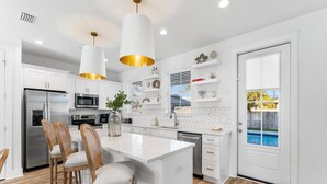 A modern kitchen with white cabinetry, stainless steel appliances, and a central island with bar stools. - Coastal Haven A by Resort Collection (Panama City Beach)