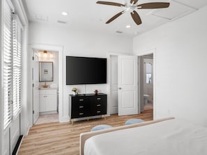 A modern bedroom with a ceiling fan, a flat-screen TV, a black dresser, and a bed with a white headboard.
