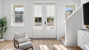 A modern living room with a white door, a sofa, a potted plant, and a staircase. - Coastal Haven A by Resort Collection (Panama City Beach)
