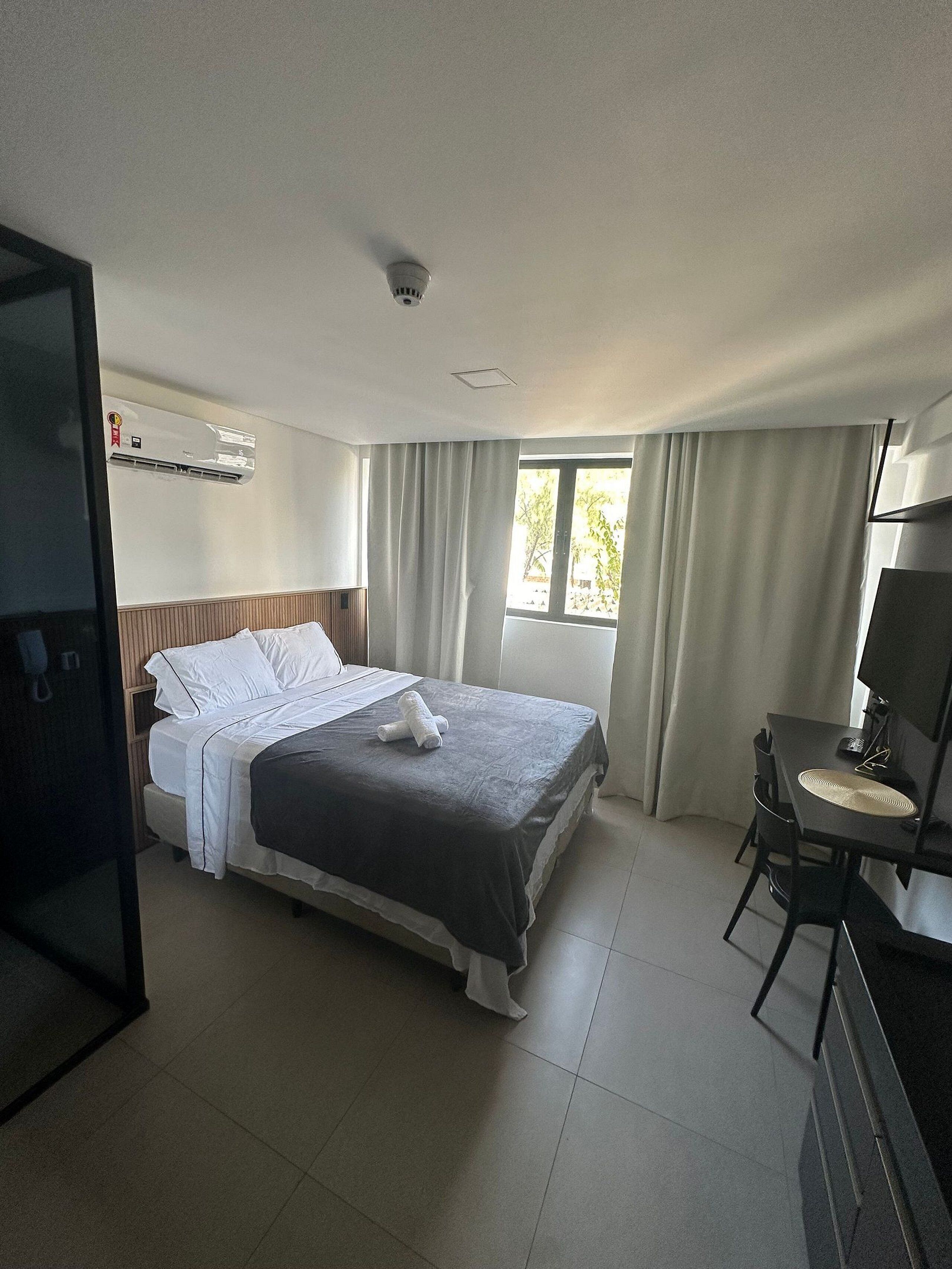 Une chambre d’hôtel comprenant un lit, un bureau avec une chaise, une fenêtre avec des rideaux et un appareil de climatisation.