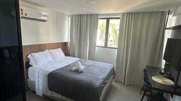 Une chambre d’hôtel comprenant un lit, un bureau avec une chaise, une fenêtre avec des rideaux et un appareil de climatisation.