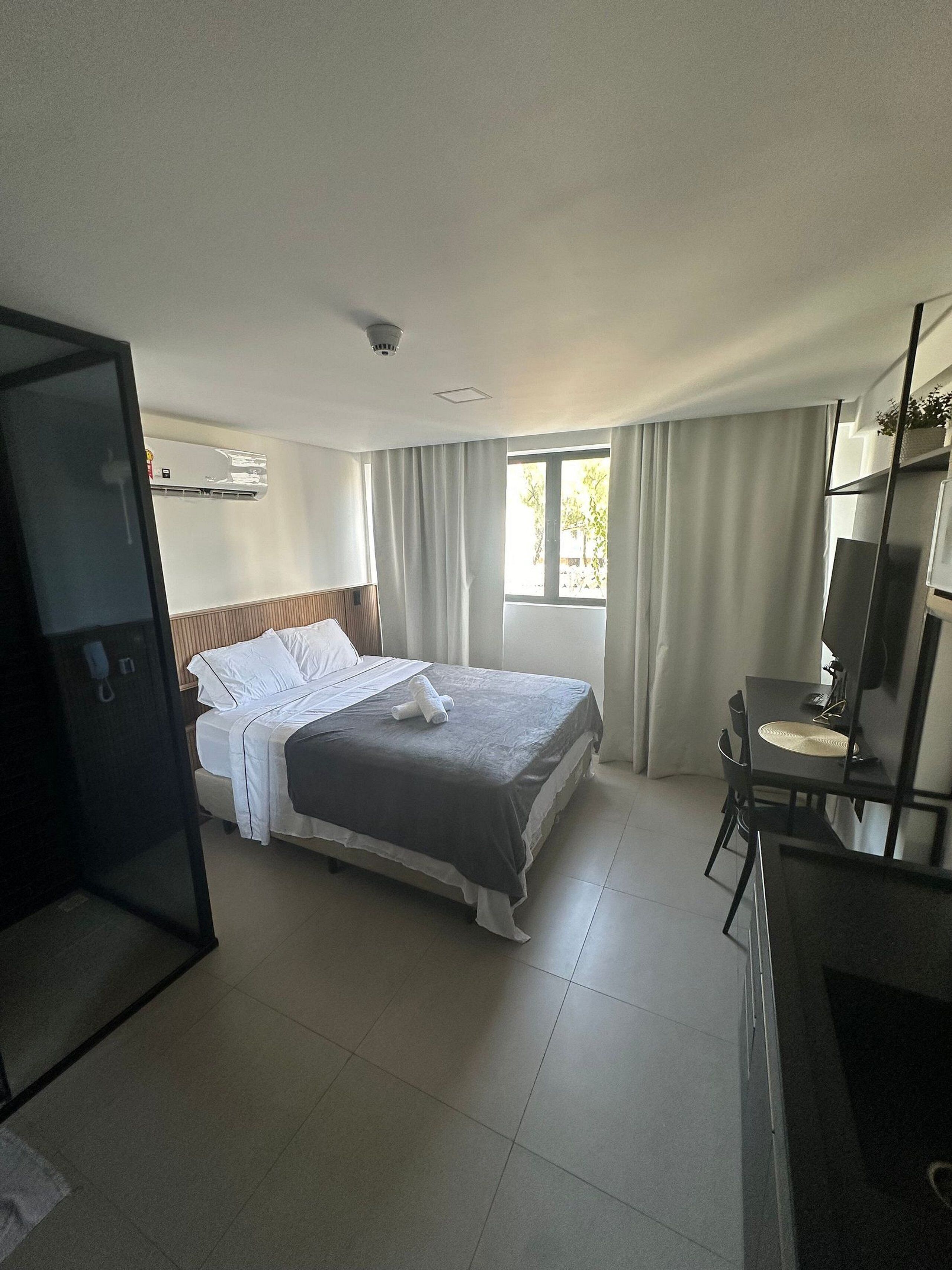 A hotel room with a bed, a desk, a chair, a wardrobe, and a window with curtains.