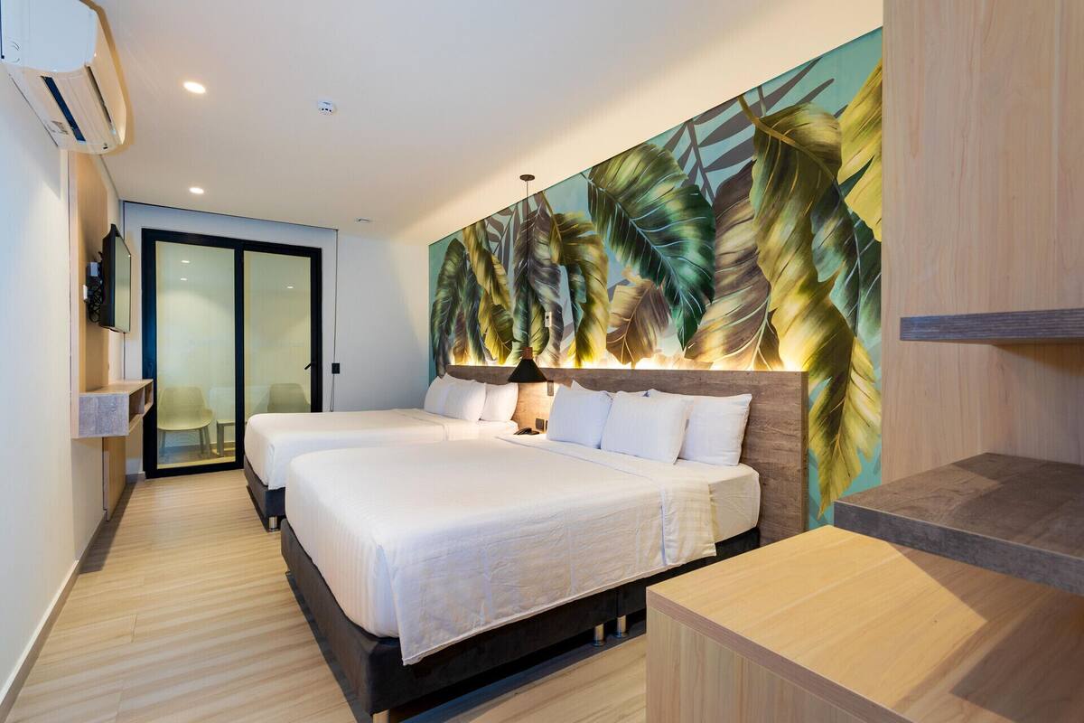 A hotel room with two beds, a large tropical leaf mural, and a modern design.