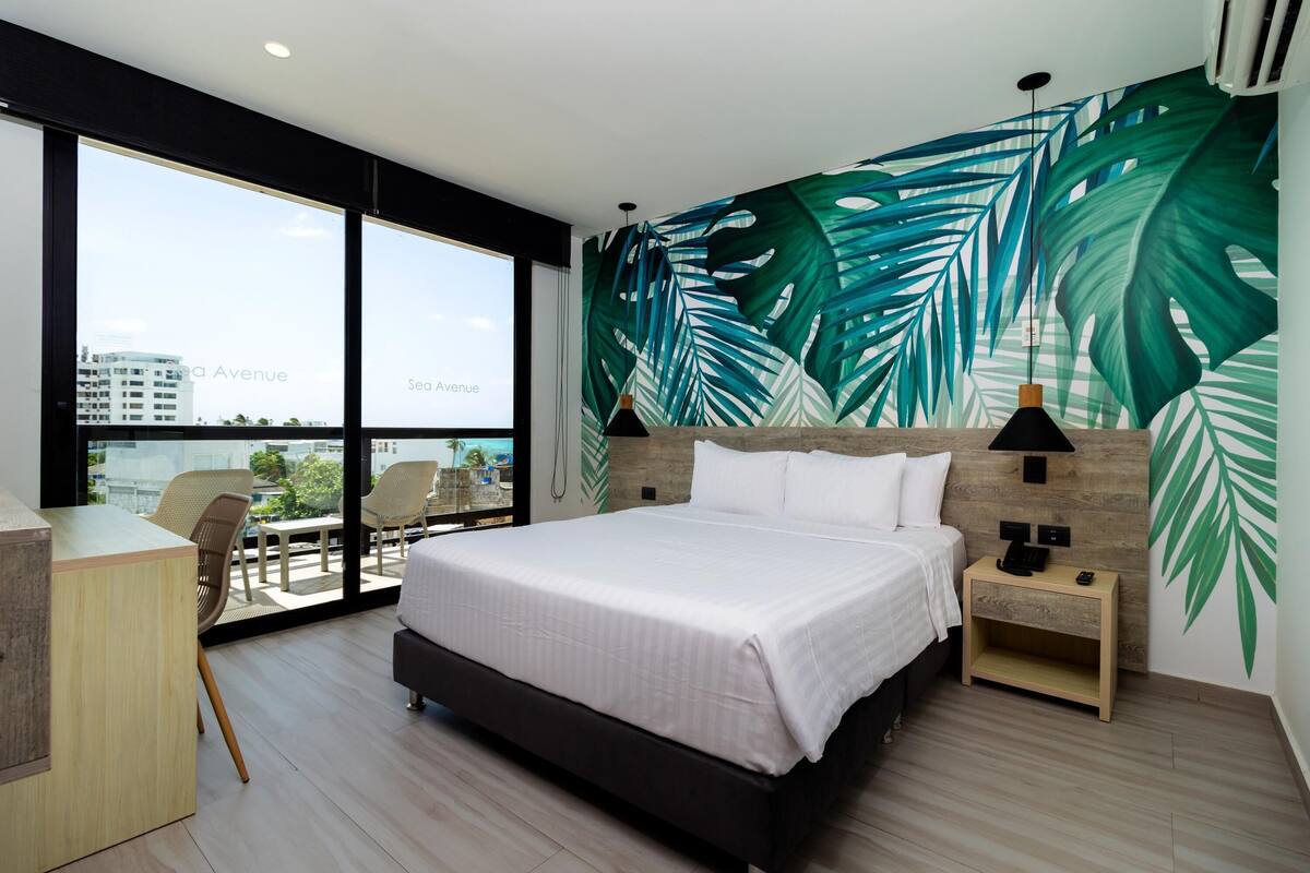 A modern hotel room with a large bed, a desk, and a view of the city.