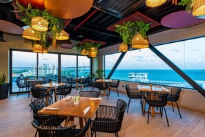 Un restaurante con terraza, amplios ventanales y lámparas de mimbre colgantes.