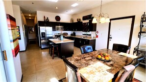 Una cocina moderna con armarios oscuros, una isla central y un comedor con mesa de mármol.