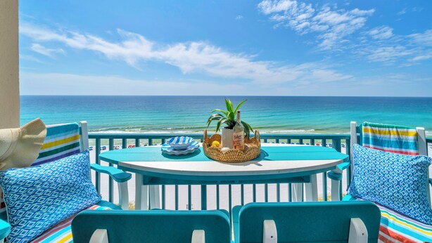 A balcony with a view of the ocean, a table with a bottle, a plant, and a basket.