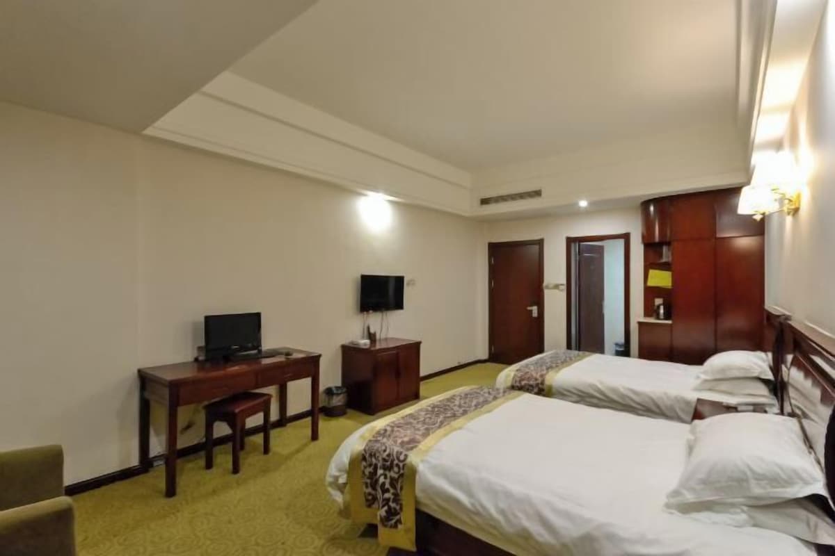 A hotel room with two beds, a desk with a chair, a television, and a wardrobe.