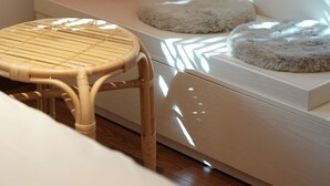 Una habitación con un banco blanco, un cojín rojo y una silla de mimbre.