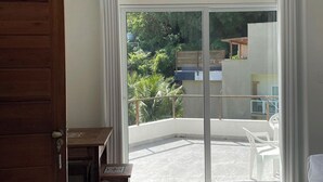 A room with a wooden door, a small table, a bench, and a view of a balcony with a white chair and a pool. - Casas de Juan (Cairu)