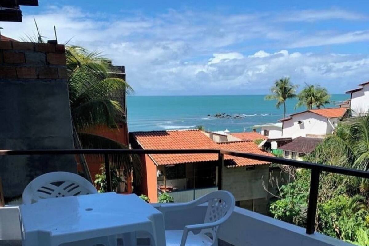 Ein Balkon mit Tisch und Stühlen, der auf eine Küstenlandschaft mit Gebäuden und Palmen blickt.