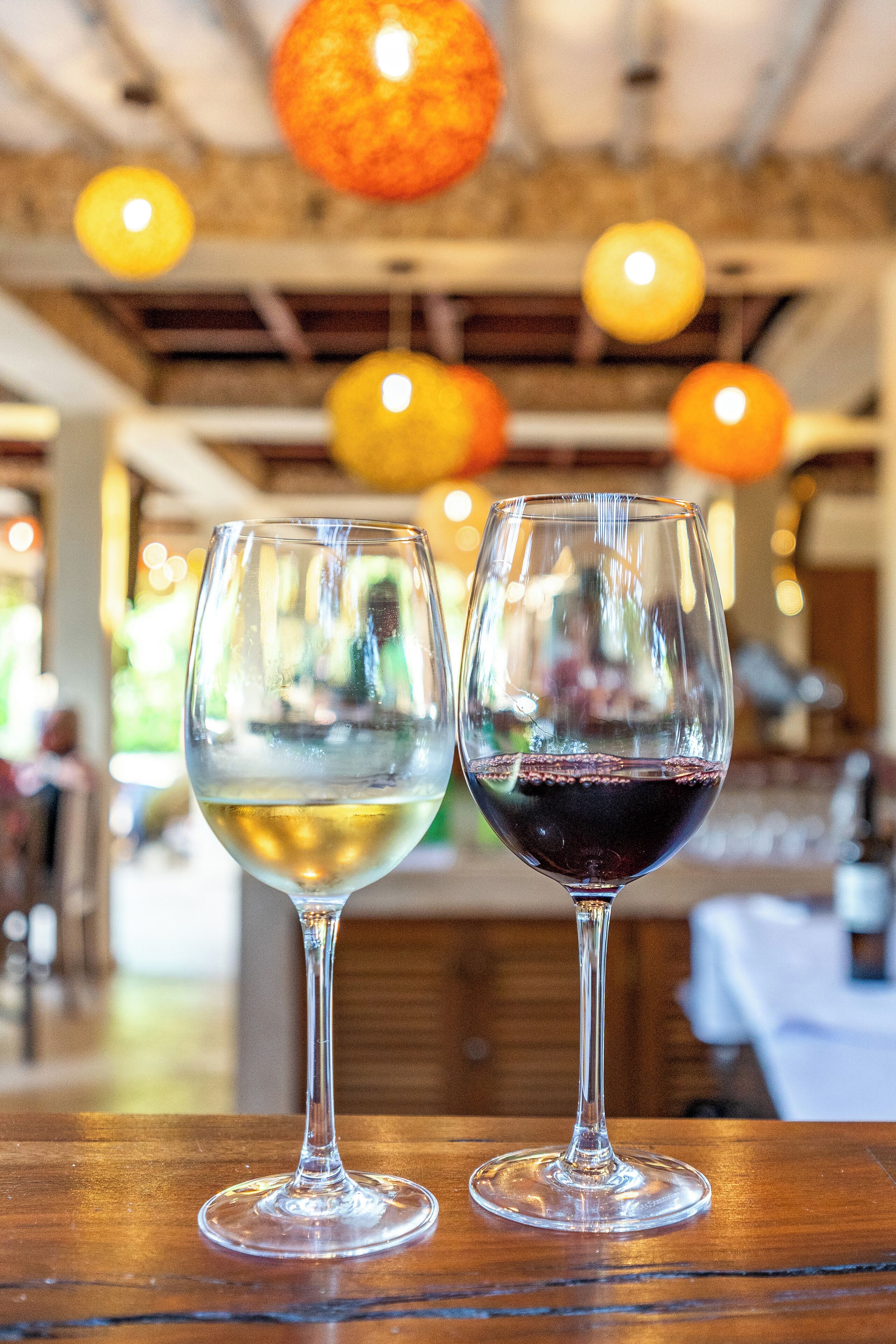 Dos copas de vino sobre una mesa de madera en un restaurante con luces colgantes.