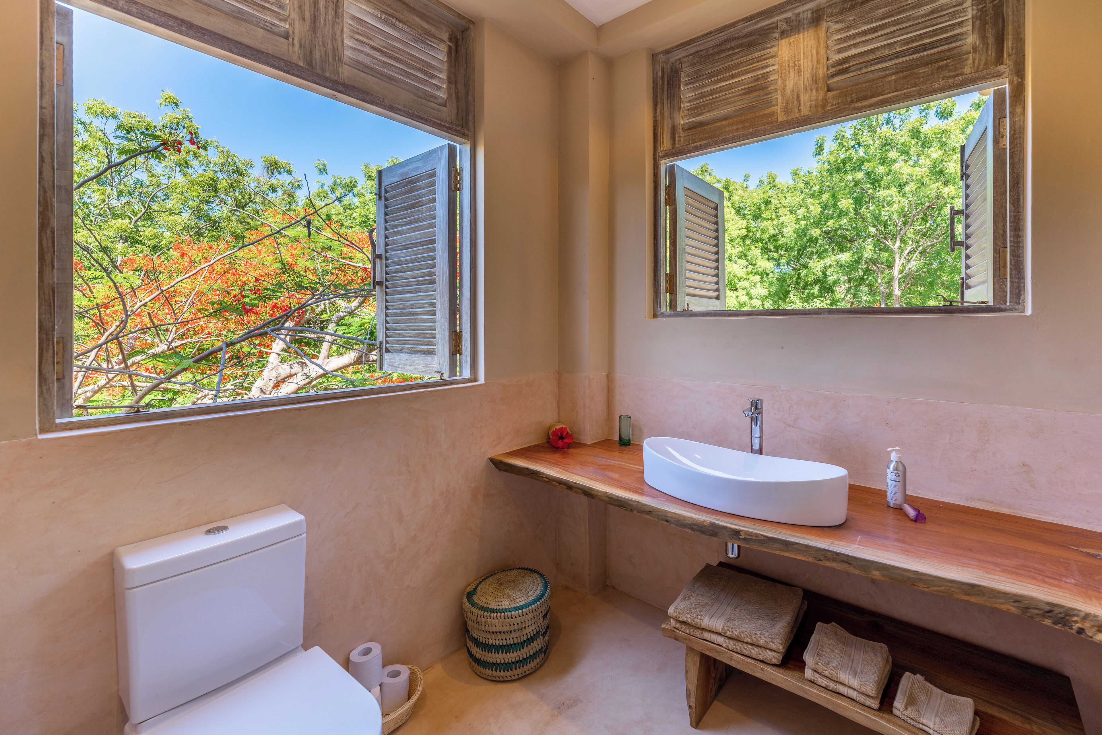 Ein Badezimmer mit Toilette, Waschbecken, Spiegel und einem Fenster mit Rollläden.