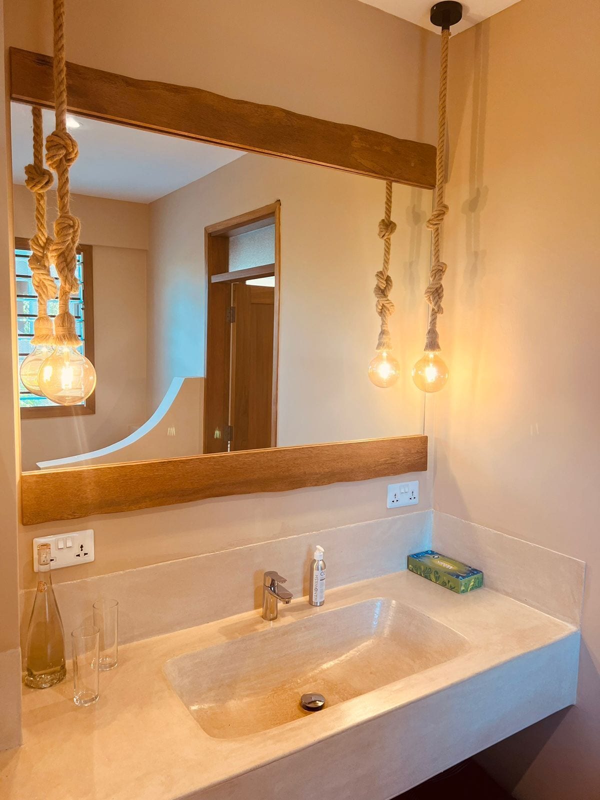 A bathroom with a wooden-framed mirror, a sink with a faucet, and two light bulbs hanging from the mirror.