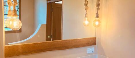 A bathroom with a wooden-framed mirror, a sink with a faucet, and two light bulbs hanging from the mirror.