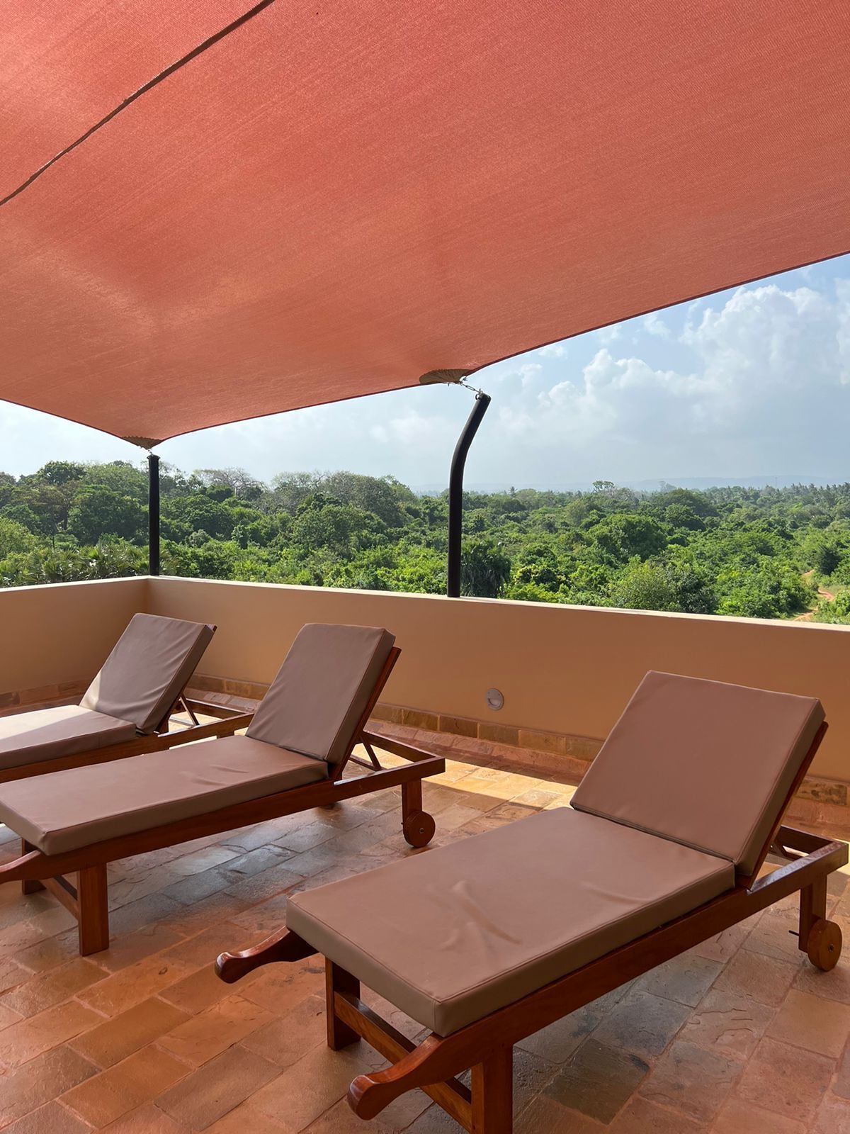 Terraço com duas cadeiras de descanso sob um toldo, com vista para uma paisagem verdejante.