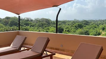 Terraço com duas cadeiras de descanso sob um toldo, com vista para uma paisagem verdejante.