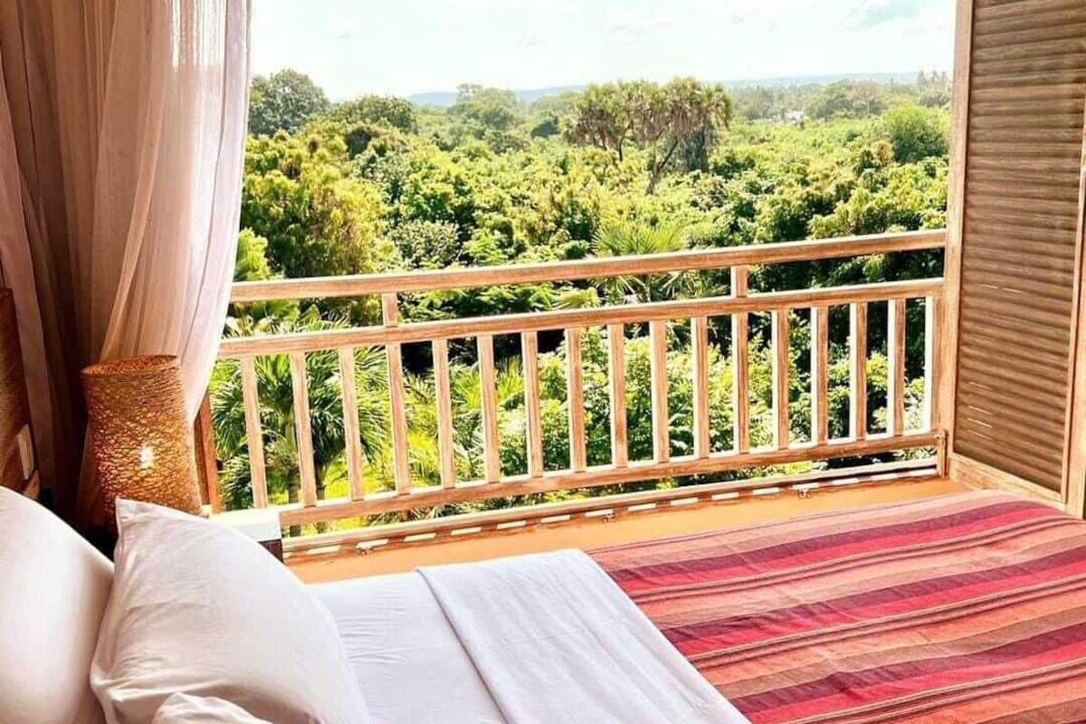 A bedroom with a bed, a view of a lush green landscape through a balcony railing.