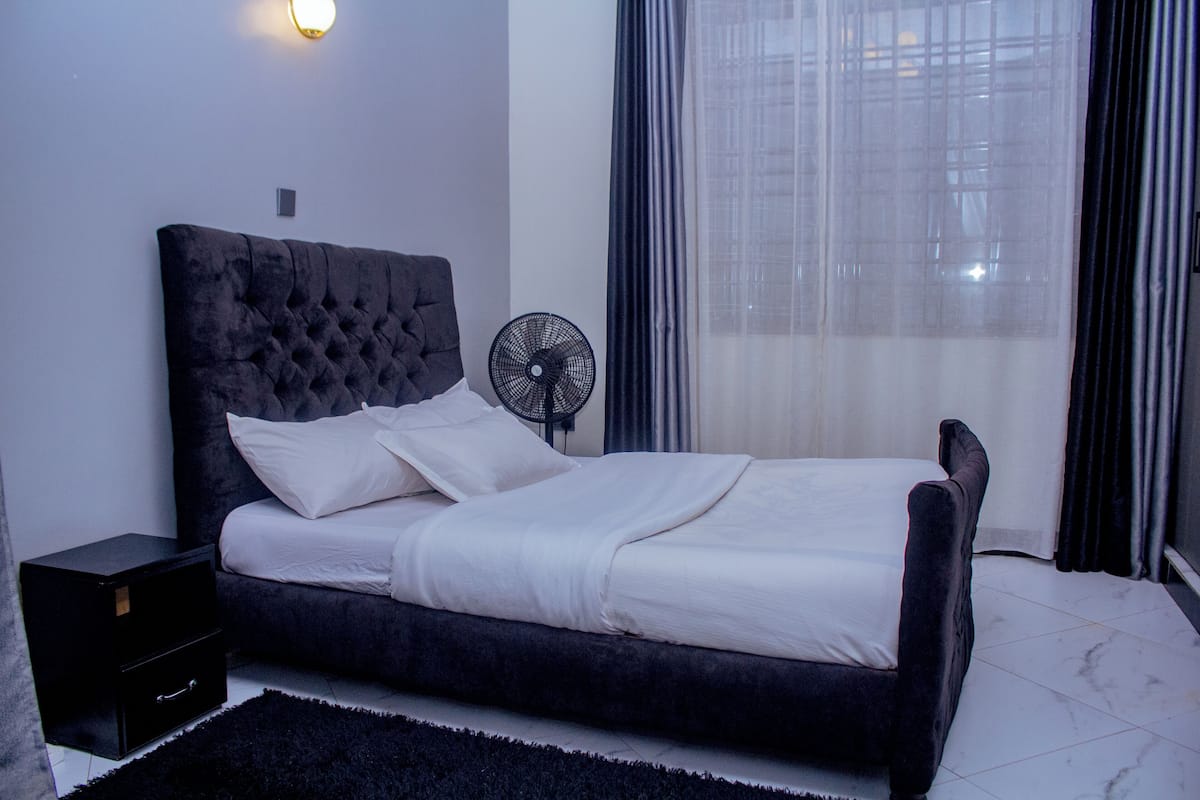 A neatly made bed with white linens, a dark headboard, and a black nightstand with a drawer.