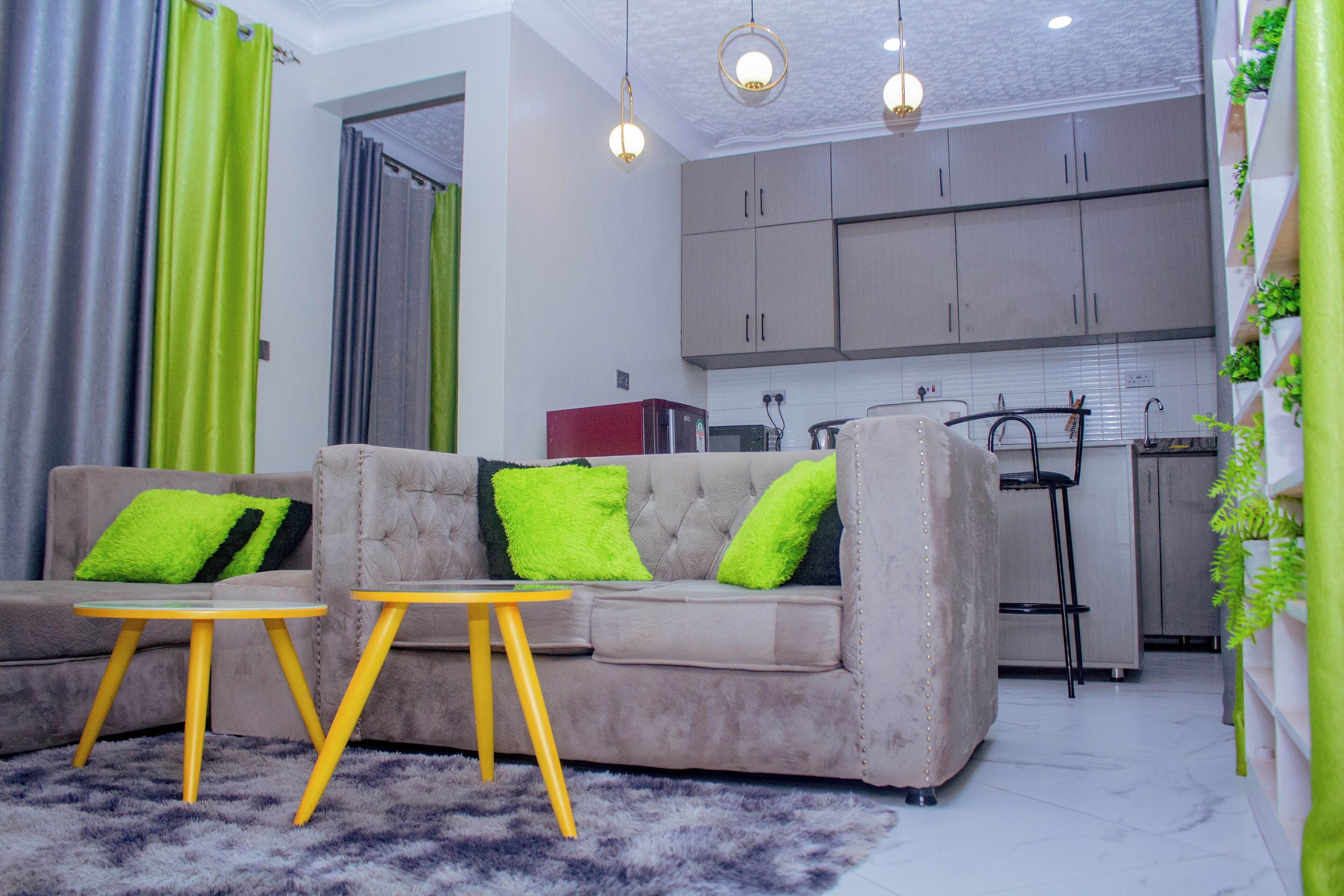 A living room with a sofa, two yellow tables, and a kitchen in the background.