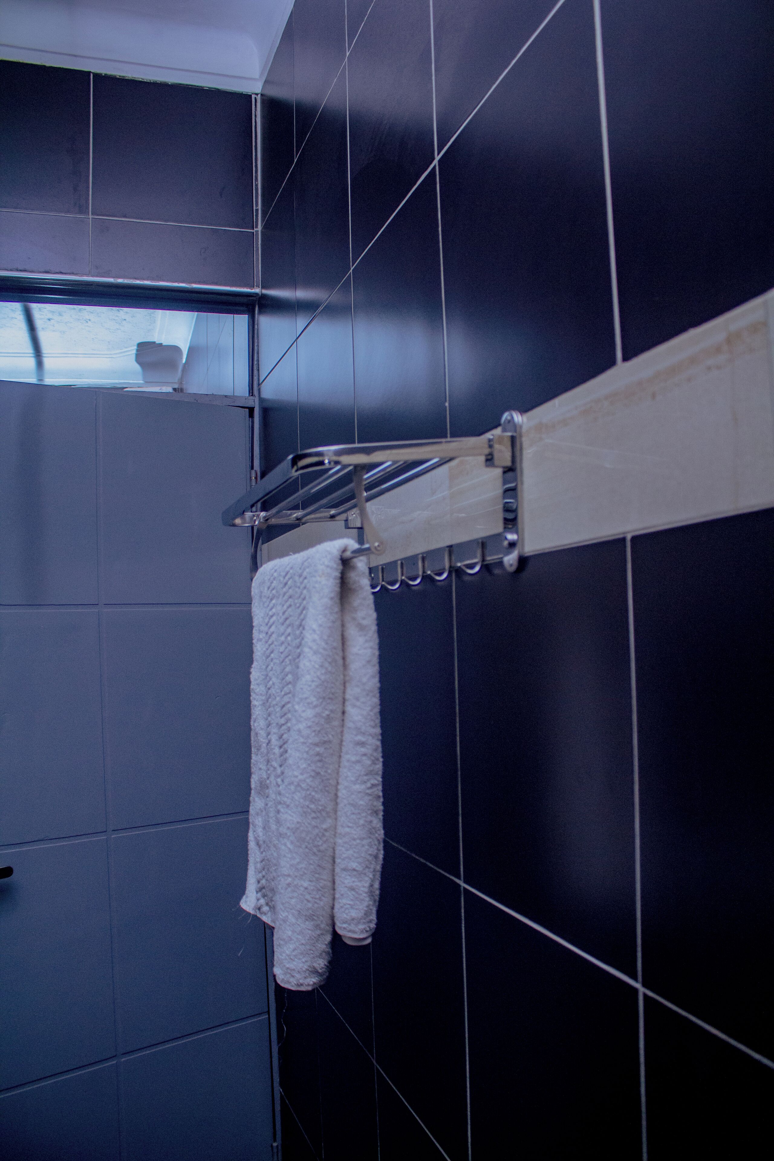 Une salle de bain avec des murs recouverts de carreaux foncés, un porte-serviettes et une serviette qui y est suspendue.