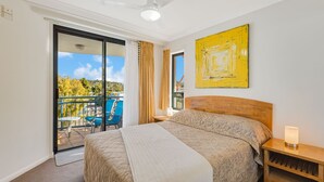 Et hotelværelse med seng, et natbord, en lampe, et stort vindue og en balkon med stole.