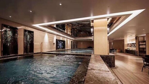 Une piscine intérieure spacieuse au design moderne, entourée d’un espace bien éclairé avec des sièges et un bar.